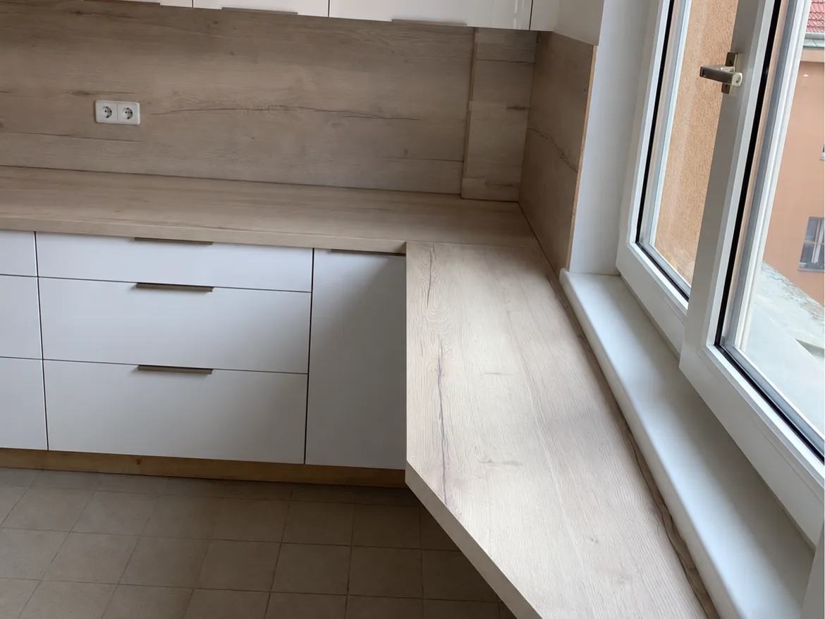 Kitchen with a wood splashback and a worktop that continues as a counter by the window