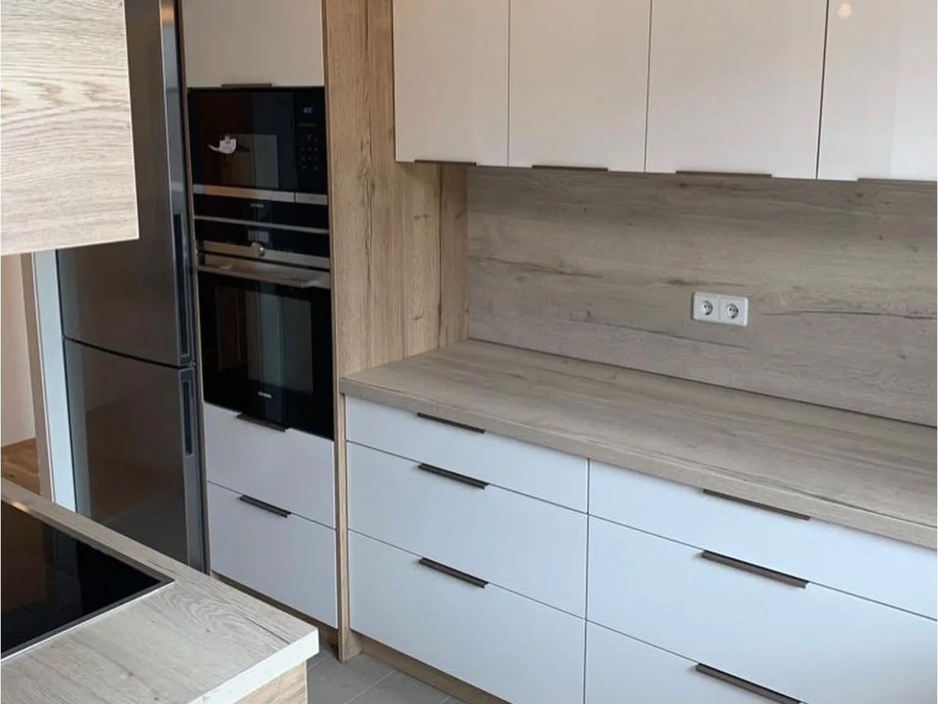 Weiße Küche mit Holzdekor-Rückwand und Hochschrank für Backofen und Mikrowelle