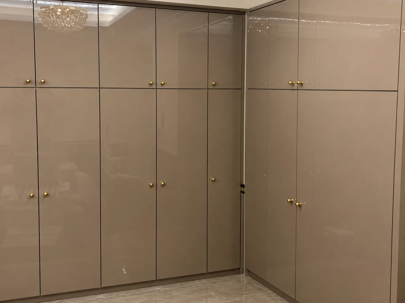 Floor-to-ceiling corner wardrobe wall in cappuccino high gloss with gold knobs